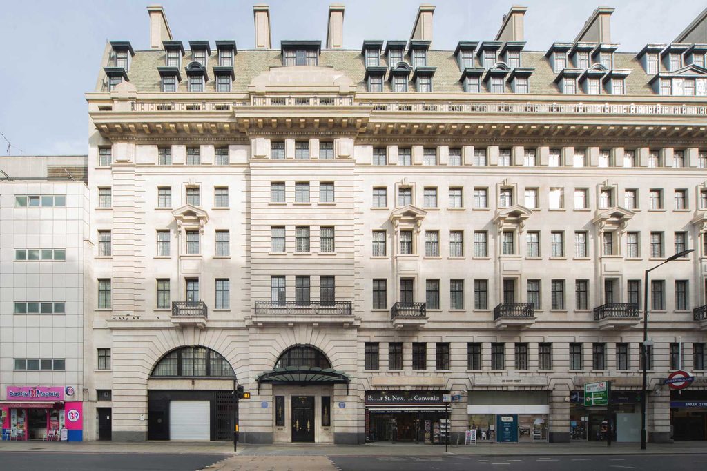 The grand stone exterior facade of Chiltern Court on Baker Street in London, featuring neo-classical architecture, a mansard roof, and ground-floor shops. Photo by Vanity Pix.