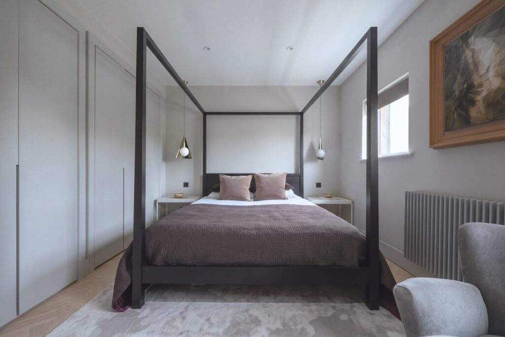 A symmetrical, eye-level shot of a modern minimalist bedroom featuring a central black four-poster bed frame. Photography by Vanity Pix.